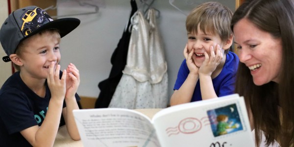 Two boys reading book with adult